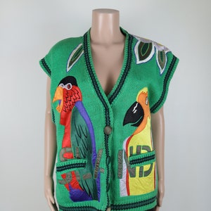 Puede incluir: Un chaleco de punto verde sin mangas con cierre de bot&oacute;n. El chaleco presenta loros bordados de colores y la palabra "Island" en la parte delantera.
