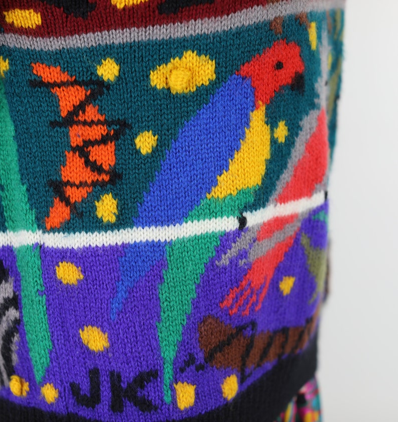 May include: A colorful knitted sweater with a parrot design. The sweater features a variety of colors, including red, blue, green, yellow, and orange. The parrot is depicted in a bright red, blue, and yellow color scheme. The sweater has a black background with a white stripe.