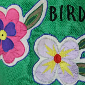 Puede incluir: Su&eacute;ter de punto verde con una aplicaci&oacute;n de flor rosa, morada y amarilla y el texto "BIRD L" en negro.