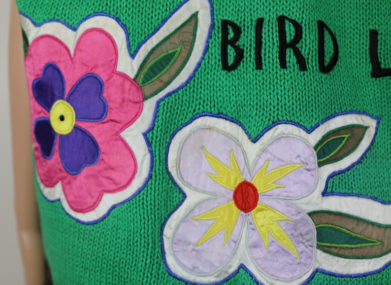 Puede incluir: Su&eacute;ter de punto verde con una aplicaci&oacute;n de flor rosa, morada y amarilla y el texto "BIRD L" en negro.