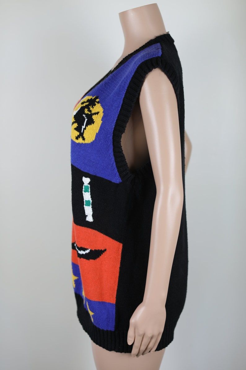 Pu&ograve; includere: Un gilet senza maniche in maglia con un motivo geometrico colorato. Il gilet &egrave; nero con accenti blu, giallo, rosso, verde e bianco.
