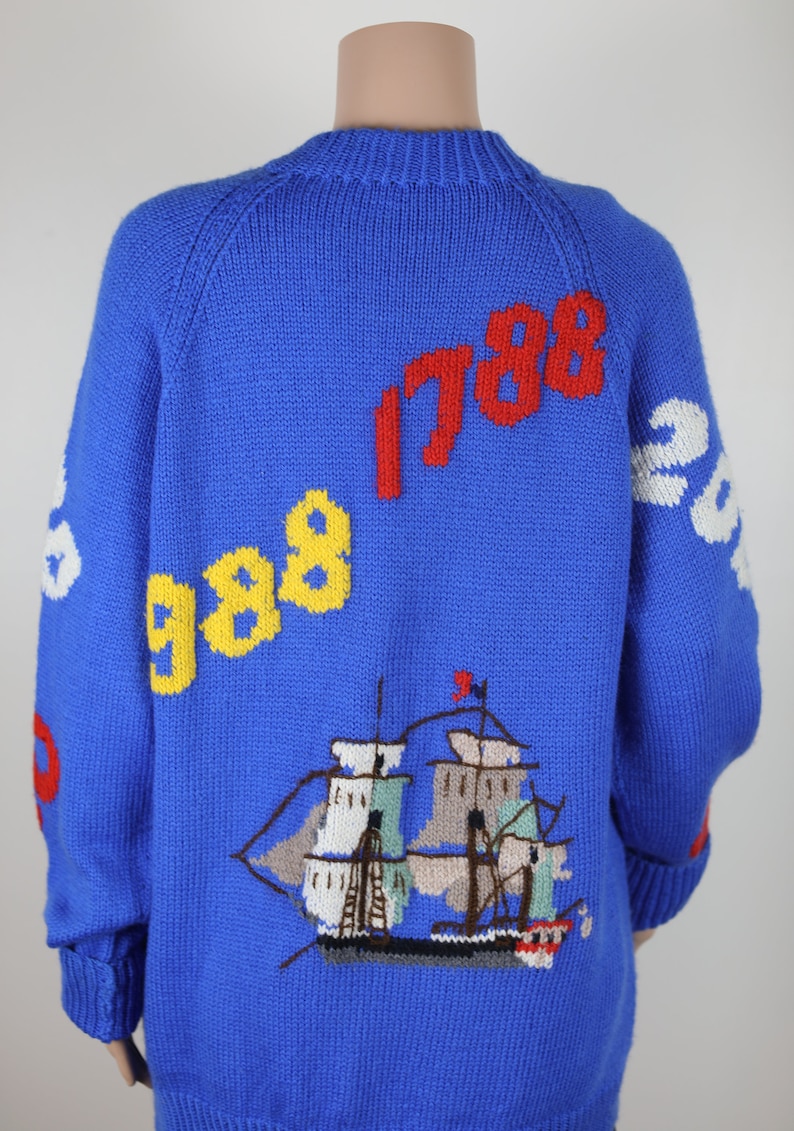 May include: Blue knitted sweater with a ship, clouds, and the numbers 1788 and 988 embroidered on it.