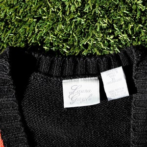 Pu&ograve; includere: Un cardigan a righe nero, rosso, bianco e blu con un'etichetta "Laura Gavazzi" e un'etichetta di cura. Il cardigan &egrave; realizzato in Corea.