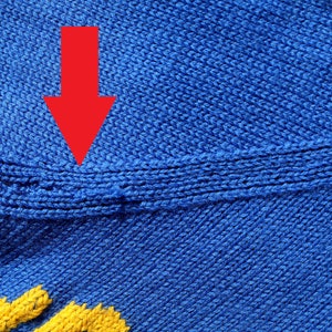 May include: Close-up of a blue knitted fabric with a seam running horizontally across the middle. The seam is highlighted by a red arrow.