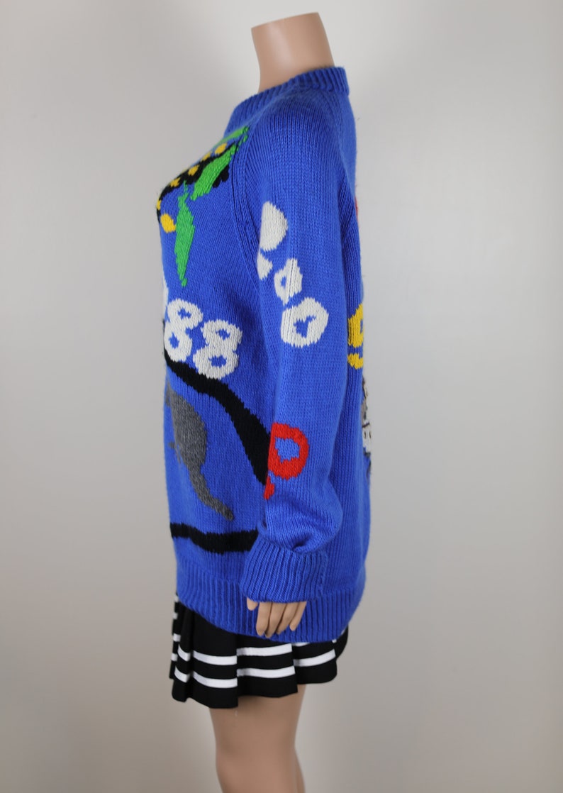 May include: A blue knitted jumper with a colourful, abstract design. The jumper has a crew neck and long sleeves.