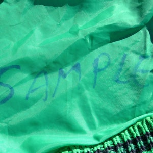 Puede incluir: Una tela verde con la palabra "SAMPLE" escrita en tinta azul.