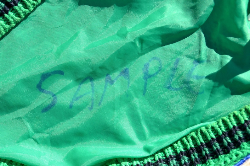 Puede incluir: Una tela verde con la palabra "SAMPLE" escrita en tinta azul.