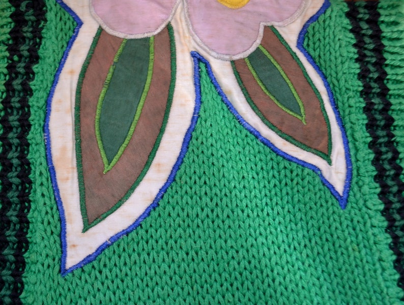 Puede incluir: Primer plano de una tela de punto verde con una aplicaci&oacute;n blanca, azul y marr&oacute;n de una flor con hojas.