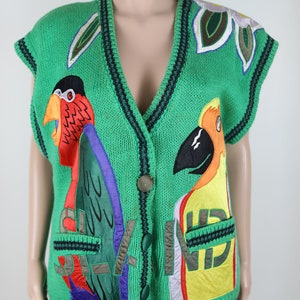 Puede incluir: Un chaleco de punto verde sin mangas con loros bordados de colores y un dise&ntilde;o floral. El chaleco tiene cierre de bot&oacute;n y dos bolsillos.