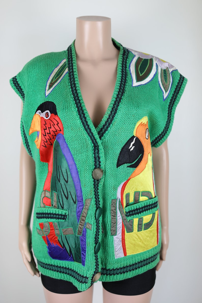 Puede incluir: Un chaleco de punto verde sin mangas con loros bordados de colores y un dise&ntilde;o floral. El chaleco tiene cierre de bot&oacute;n y dos bolsillos.