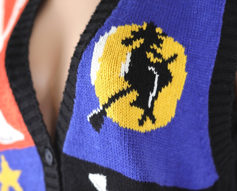 Pu&ograve; includere: Un gilet di maglia nero, blu, rosso, bianco e giallo con una strega che vola su una scopa davanti a un grafico di luna gialla.
