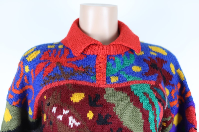 May include: A colorful knitted sweater with a red collar and three button closure. The sweater features a geometric pattern in shades of red, blue, green, yellow, and brown.