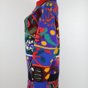 May include: A colorful, multi-patterned sweater with a crew neck. The sweater features a variety of geometric shapes, animals, and abstract designs in red, blue, green, yellow, and black.