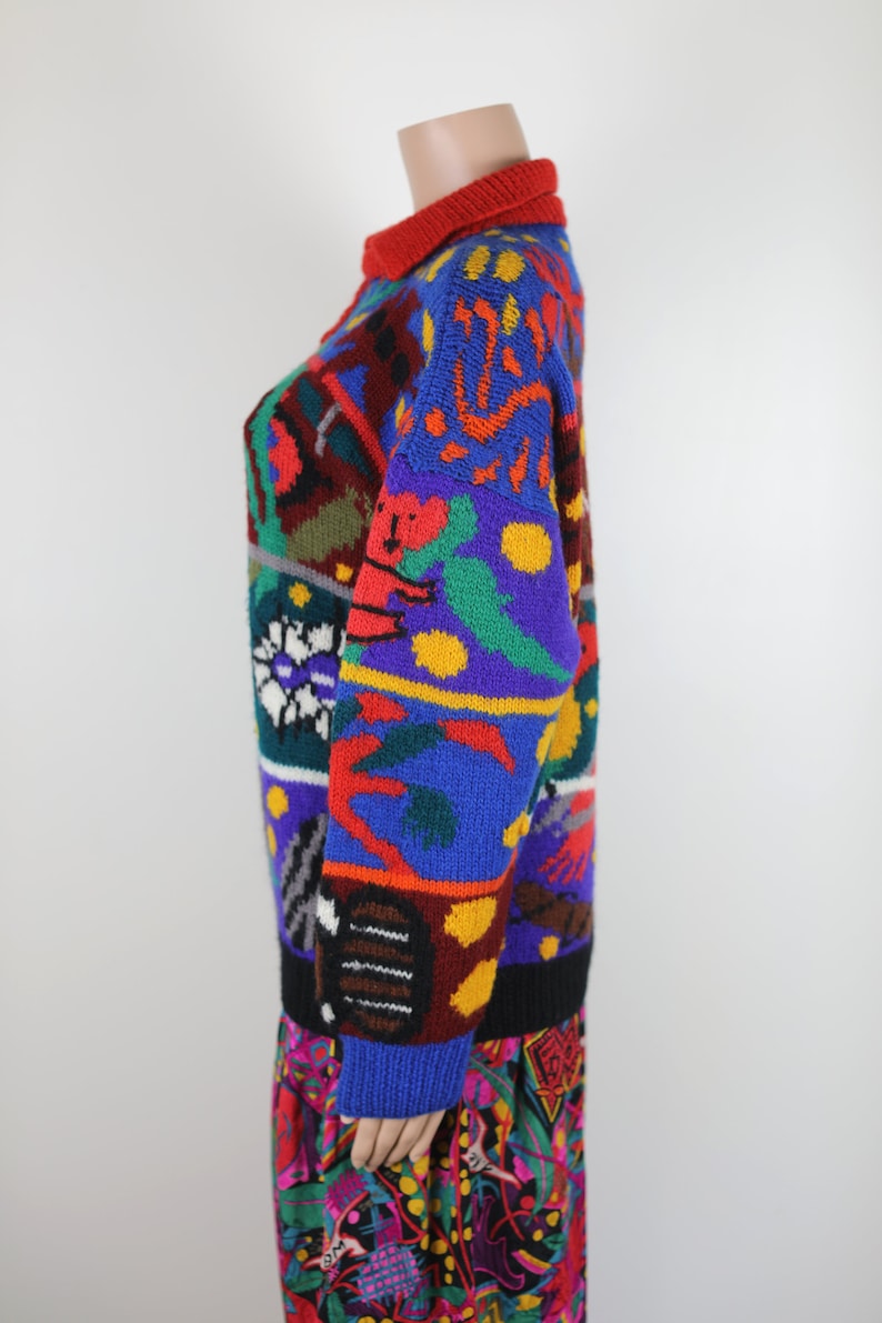 May include: A colorful, multi-patterned sweater with a crew neck. The sweater features a variety of geometric shapes, animals, and abstract designs in red, blue, green, yellow, and black.
