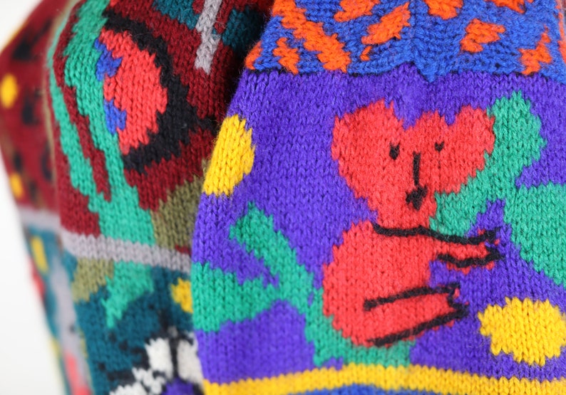 May include: A colorful knitted sweater with a red koala bear design. The sweater features a variety of colors, including red, blue, green, yellow, and purple.