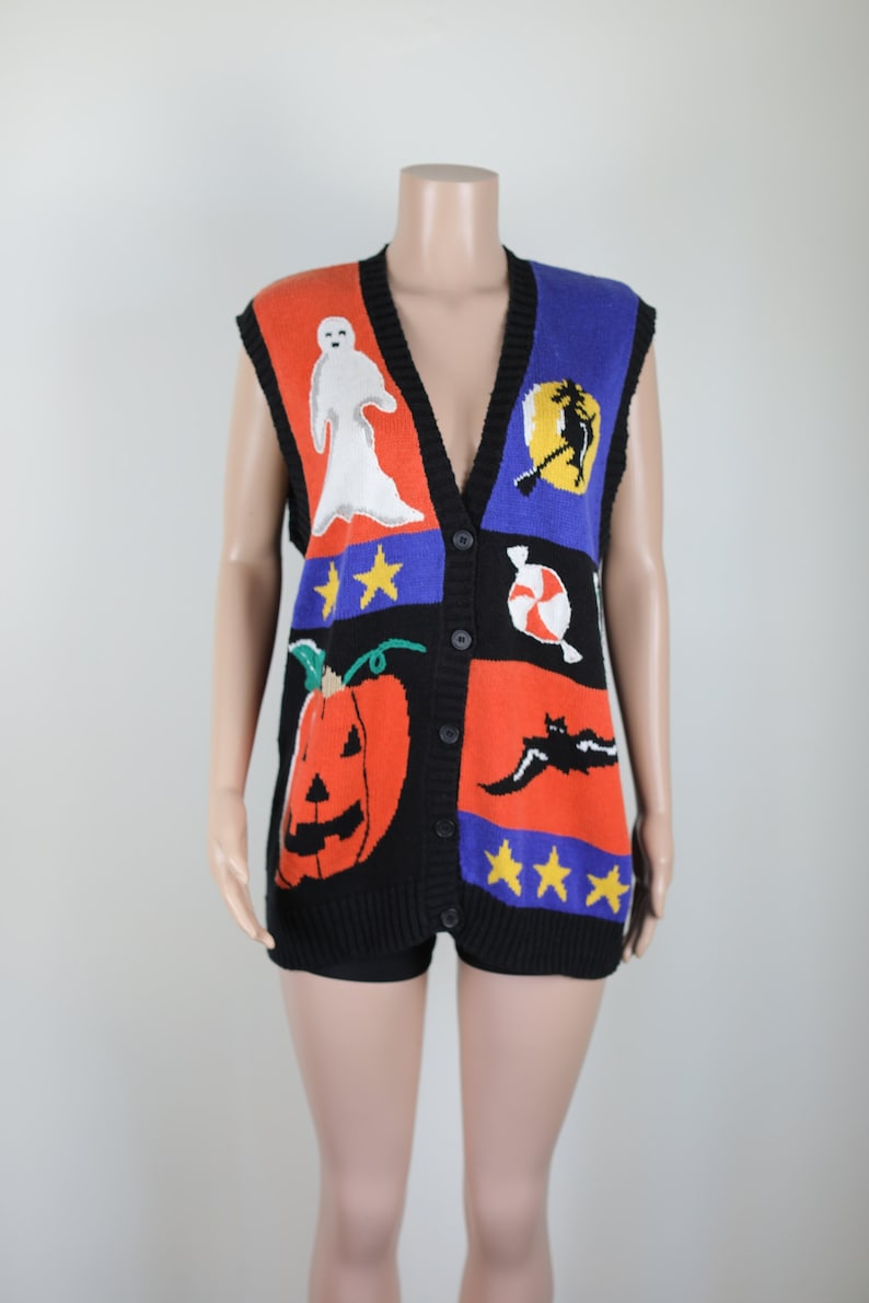 Pu&ograve; includere: Un gilet di maglina nero senza maniche con un design di Halloween colorato. Il gilet presenta una zucca, un fantasma, un pipistrello, una strega, una canna di zucchero e stelle.