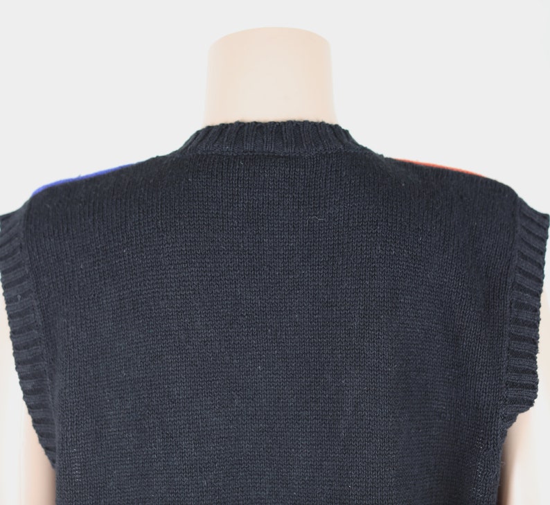 Pu&ograve; includere: Gilet di maglia nero senza maniche con un bordo blu e rosso intorno al collo.