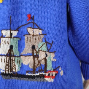 May include: A blue knitted jumper with a colourful embroidered ship design on the back. The ship has white, brown and green sails and a red flag.
