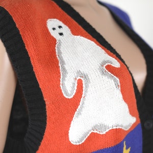 Pu&ograve; includere: Un gilet di maglia rosso, nero, blu e giallo con un disegno di fantasma bianco. Il gilet ha un collo a V e una chiusura con bottoni.