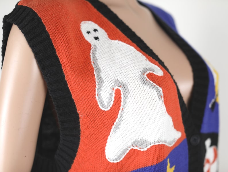 Pu&ograve; includere: Un gilet di maglia rosso, nero, blu e giallo con un disegno di fantasma bianco. Il gilet ha un collo a V e una chiusura con bottoni.