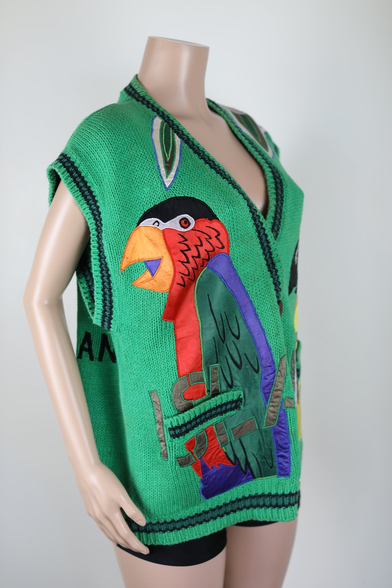 Puede incluir: Su&eacute;ter verde sin mangas con un dise&ntilde;o de loro y la palabra "Island" en la parte delantera. El loro est&aacute; hecho de tela colorida y tiene un pico grande.