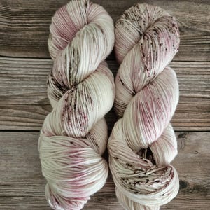 May include: Two skeins of yarn in a white and pink colourway with brown speckles. The yarn is soft and fluffy and would be perfect for knitting or crocheting.
