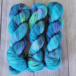 May include: Three skeins of teal, green, and purple hand-dyed yarn. The yarn is arranged in a loose braid.