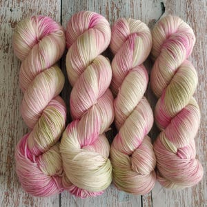 May include: Four skeins of yarn in a soft, pastel color palette. The yarn is a blend of pink, cream, and light green, creating a visually appealing texture. The skeins are arranged in a row, showcasing the color variations.