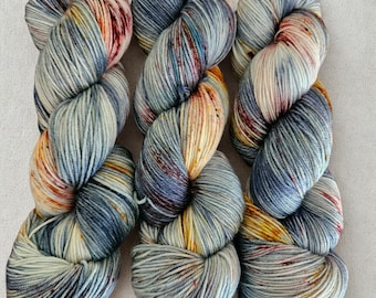 Puede incluir: Tres madejas de hilo teñido a mano en una paleta de colores azul claro, crema y óxido. El hilo está torcido en forma de madeja, con variaciones visibles de color y textura. El hilo probablemente está hecho de lana o una fibra similar, adecuado para proyectos de tejido o ganchillo.