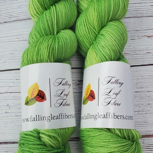 May include: Two skeins of green yarn with a gradient of color. The yarn is labeled "Falling Leaf Fibers" and includes a website address.