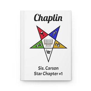 May include: A white journal with the word "Chaplin" in black script at the top. Below is a colorful star emblem with a book in the center and the text "Sis. Carson Star Chapter #1" at the bottom.