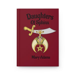 May include: A maroon journal with the words "Daughters Of Sphinx" in black script. A gold and silver sword and pendant design is centered on the cover, with the name "Mary Adams" below.