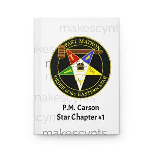 May include: A white journal featuring a circular emblem with the text "PAST MATRON" and "ORDER of the EASTERN STAR." The emblem is black and gold with a star design. Below the emblem is the text "P.M. Carson Star Chapter #1."