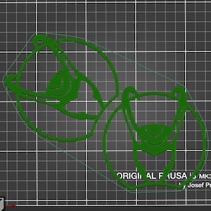 Pode incluir: Dois stencils de parede decorativos de cor verde, cortados a laser, em forma de rosto estilizado com uma coroa. Os stencils estão sobre um fundo de grade cinza. O texto "ORIGINAL FRUSA" é visível na parte inferior da imagem.