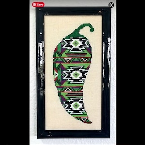 May include: A framed cross-stitch of a green chili pepper with a geometric pattern in black, white, red, and green.