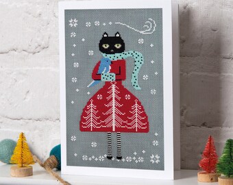 May include: A greeting card featuring a black cat wearing a red dress and a blue scarf, holding a blue bird. The cat is standing in a snowy forest with white snowflakes on a grey background.