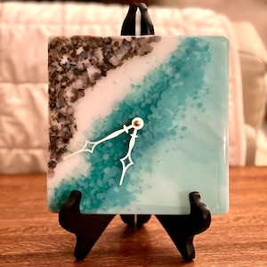 May include: A teal, white, and brown abstract art clock with gold hands on a black easel stand.