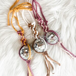 May include: Three handmade macrame keychains with silver disco ball ornaments. The keychains are made with brown, white and pink yarn.