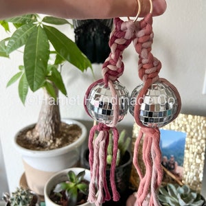 May include: Two pink and red macrame keychains with silver disco ball charms. The keychains are tied together with a gold ring.
