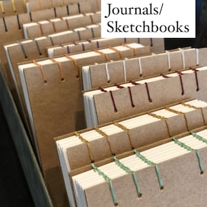 May include: A stack of hand-bound journals and sketchbooks with different colored stitching. The text "Hand bound Journals/Sketchbooks" is visible at the top of the image.