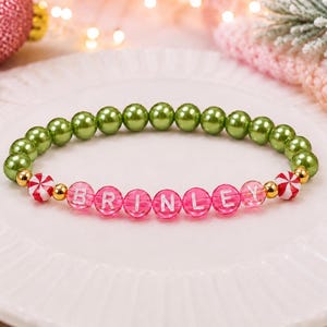 Puede incluir: Una pulsera de cuentas con una hilera de cuentas redondas de color verde oliva met&aacute;lico, seguida de una secci&oacute;n de cuentas de color rosa intenso transl&uacute;cido con el nombre BRINLEY en letras blancas, con espaciadores dorados y cuentas de menta.