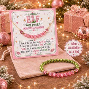 Puede incluir: Un collar de cadena dorada con cuentas de letras rosas que forman el nombre BRINLEY y cuentas de menta rojas y blancas sobre una tarjeta que dice A SPECIAL ELF DELIVERY FROM SANTA'S WORKSHOP, junto a una pulsera a juego con cuentas verdes y rosas.