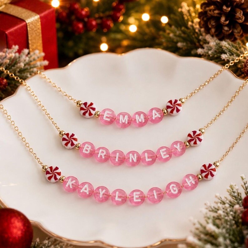 Puede incluir: Tres collares de cadena dorada con cuentas de letras rosas transl&uacute;cidas que deletrean los nombres EMMA, BRINLEY y KAYLEIGH. Cada collar est&aacute; decorado con cuentas redondas blancas y rojas con patr&oacute;n de menta en los extremos.