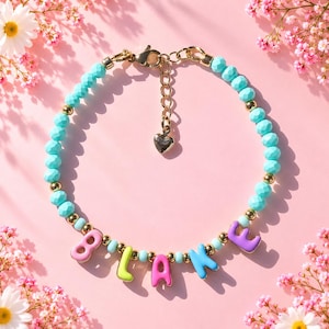 May include: A beaded bracelet featuring faceted turquoise beads, small gold-tone metallic beads, and colorful letter beads spelling the name BLAKE. The bracelet includes a gold-tone lobster claw clasp, an extender chain, and a small heart charm.