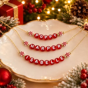 Puede incluir: Tres collares de cadena dorada con cuentas de letras de acr&iacute;lico rojo que forman los nombres Poppy, Harper e Isabelle. Cada collar est&aacute; decorado con peque&ntilde;as cuentas redondas de patr&oacute;n de menta roja y blanca a ambos lados.