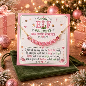 Puede incluir: Un collar de cadena dorada con cuentas de letras rosas que forman el nombre BRINLEY, presentado en una tarjeta blanca con el texto A SPECIAL ELF DELIVERY FROM SANTA'S WORKSHOP y un poema sobre un regalo del Polo Norte, con detalles rojos y verdes.