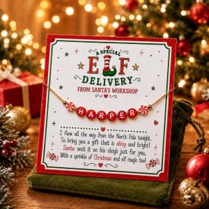Puede incluir: Un collar de cuentas dorado con cuentas de letras rojas que deletrean HARPER y cuentas de caramelo de menta, presentado en una tarjeta blanca con bordes verdes y rojos. El texto dice A SPECIAL ELF DELIVERY FROM SANTA'S WORKSHOP.