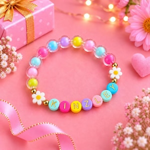 Peut inclure: Un bracelet élastique composé de perles translucides colorées, de perles lettres opaques formant le mot KINZLEY et de perles en forme de fleurs blanches à cœur jaune. Le design inclut de petites perles intercalaires dorées.