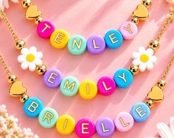 May include: Three gold-tone chain necklaces featuring colorful round letter beads spelling the names TENLEY, EMILY, and BRIELLE. Each necklace is accented with gold-tone heart beads, small gold-tone spacer beads, and white daisy flower charms.