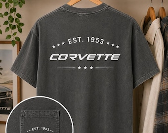 May include: A charcoal grey short-sleeve t-shirt featuring a white graphic on the back that reads EST. 1953 CORVETTE with stars. A circular inset shows a matching pocket on the front with the same white text and star design printed on the fabric.
